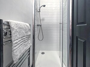 Et brusebad med glasdør, hvide flisevægge og et hvidt håndklæde på en holder.