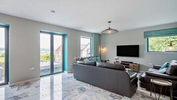 A modern living room with a large sofa, a television, and a balcony with a view.
