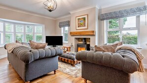 A living room with two grey sofas, a flat-screen TV, a fireplace, and large windows. - 4 Bed in Middlesbrough (oc-96213) (Great Broughton)