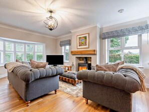 Ein Wohnzimmer mit zwei grauen Sofas, einem Flachbildfernseher, einem Kamin und großen Fenstern.