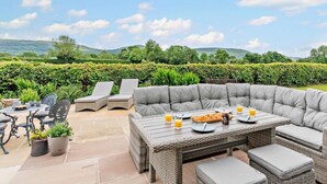 An outdoor seating area with a wicker table and chairs, a view of a vineyard, and a hilly landscape in the background. - 4 Bed in Middlesbrough (oc-96213) (Great Broughton)