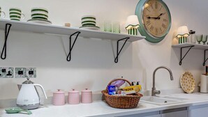 A kitchen with a white countertop, a kettle, pink containers, a basket with food items, and a clock on the wall. - 1 Bed in Gateshead (oc-95877) (Lamesley)