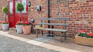 A brick building with a red door, a bench, and potted plants. - 1 Bed in Gateshead (oc-95877) (Lamesley)