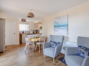 A modern living room with a dining area, a kitchen in the background, and a large painting on the wall. - 2 Bed in Taunton (oc-96234) (West Quantoxhead)