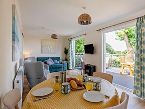 A dining area with a table set for breakfast, a sofa, and a TV in the background. - 2 Bed in Taunton (oc-96234) (West Quantoxhead)