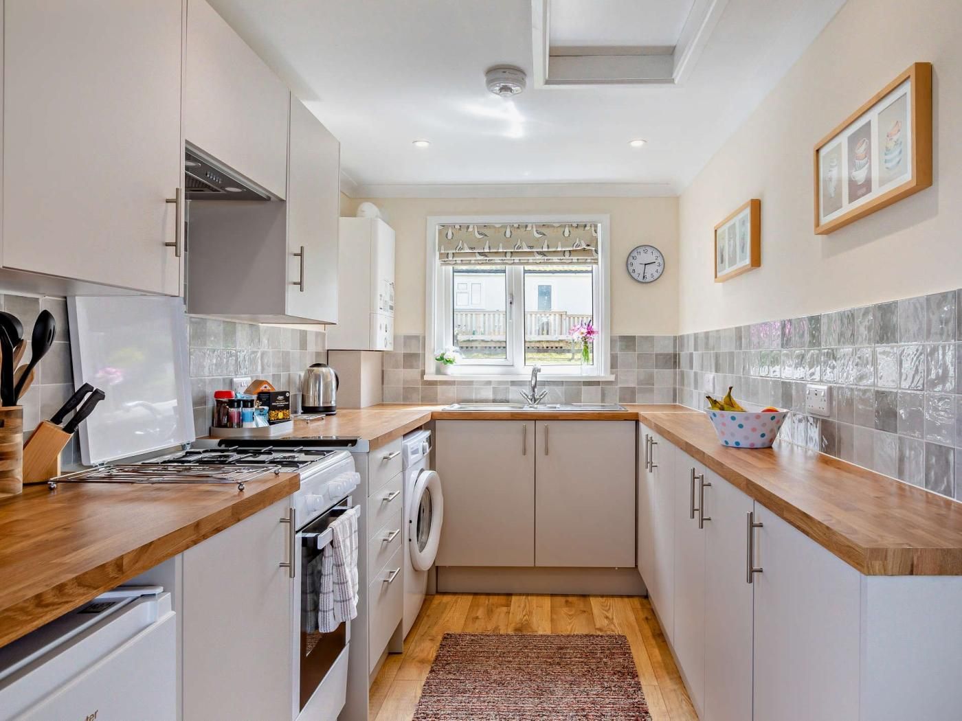 A modern kitchen with a stove, oven, and washing machine, wooden countertops, and a window with a view.