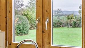 Ein schmiedeeiserner Fensterrahmen mit Blick auf einen gepflegten Garten und eine entfernte Landschaft.