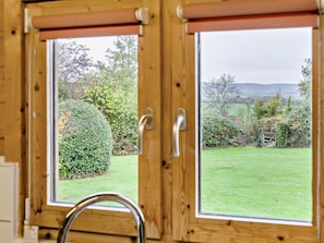 Ein schmiedeeiserner Fensterrahmen mit Blick auf einen gepflegten Garten und eine entfernte Landschaft.