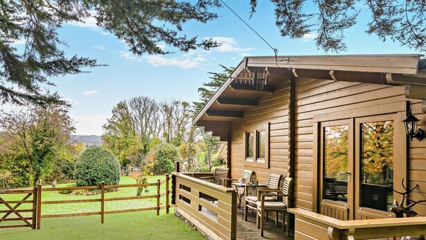 Eine Holzhütte mit Veranda, Sitzgelegenheiten im Freien und einem eingezäunten Garten.