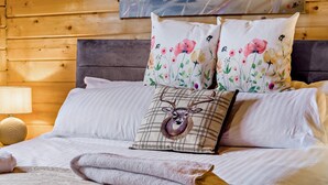 Ein Bett mit einem karo-Kissen mit einem Hirschmotiv, einem Blumenkissen und einem aufgerollten Handtuch.