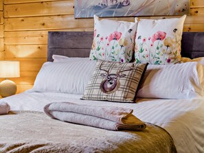 Ein Bett mit einem karo-Kissen mit einem Hirschmotiv, einem Blumenkissen und einem aufgerollten Handtuch.