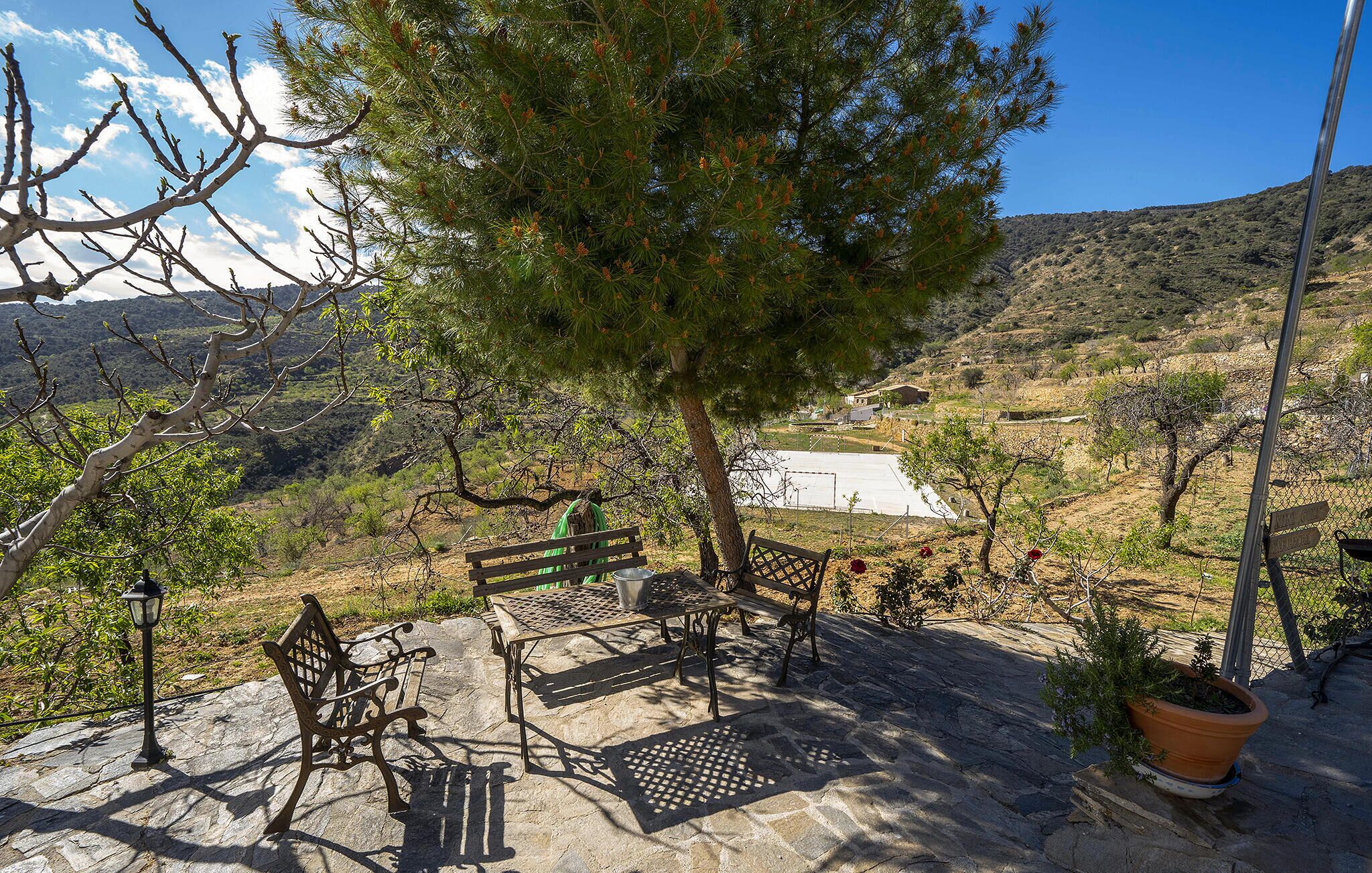 A patio with outdoor furniture, a tree, and a view of a hilly landscape.