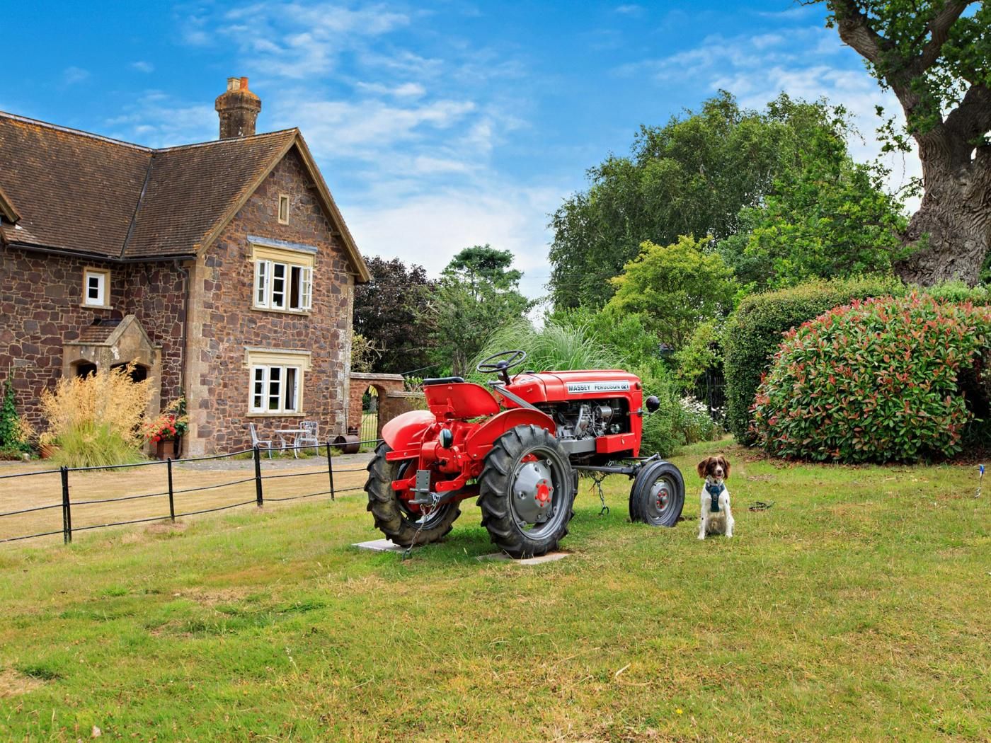 Une maison en pierre avec un tracteur rouge garé devant.