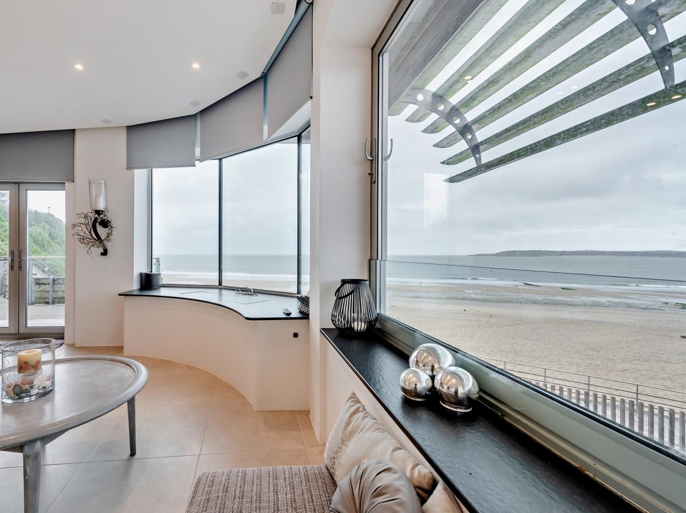 A modern interior with a curved bench, a table with a candle, and a view of the beach through large windows.