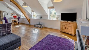 A spacious loft with high ceilings, exposed wooden beams, a large TV, and a cozy seating area. - 1 Bed in Inverkeithing (oc-96221) (Inverkeithing)