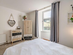 A bedroom with a bed, a dresser, a wardrobe, a mirror, a window with curtains, and a wall-mounted shelf with a plant. - 1 Bed in Inverkeithing (oc-96221) (Inverkeithing)
