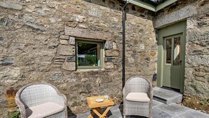 Un bâtiment en pierre avec deux chaises en osier et une petite table à l’extérieur.