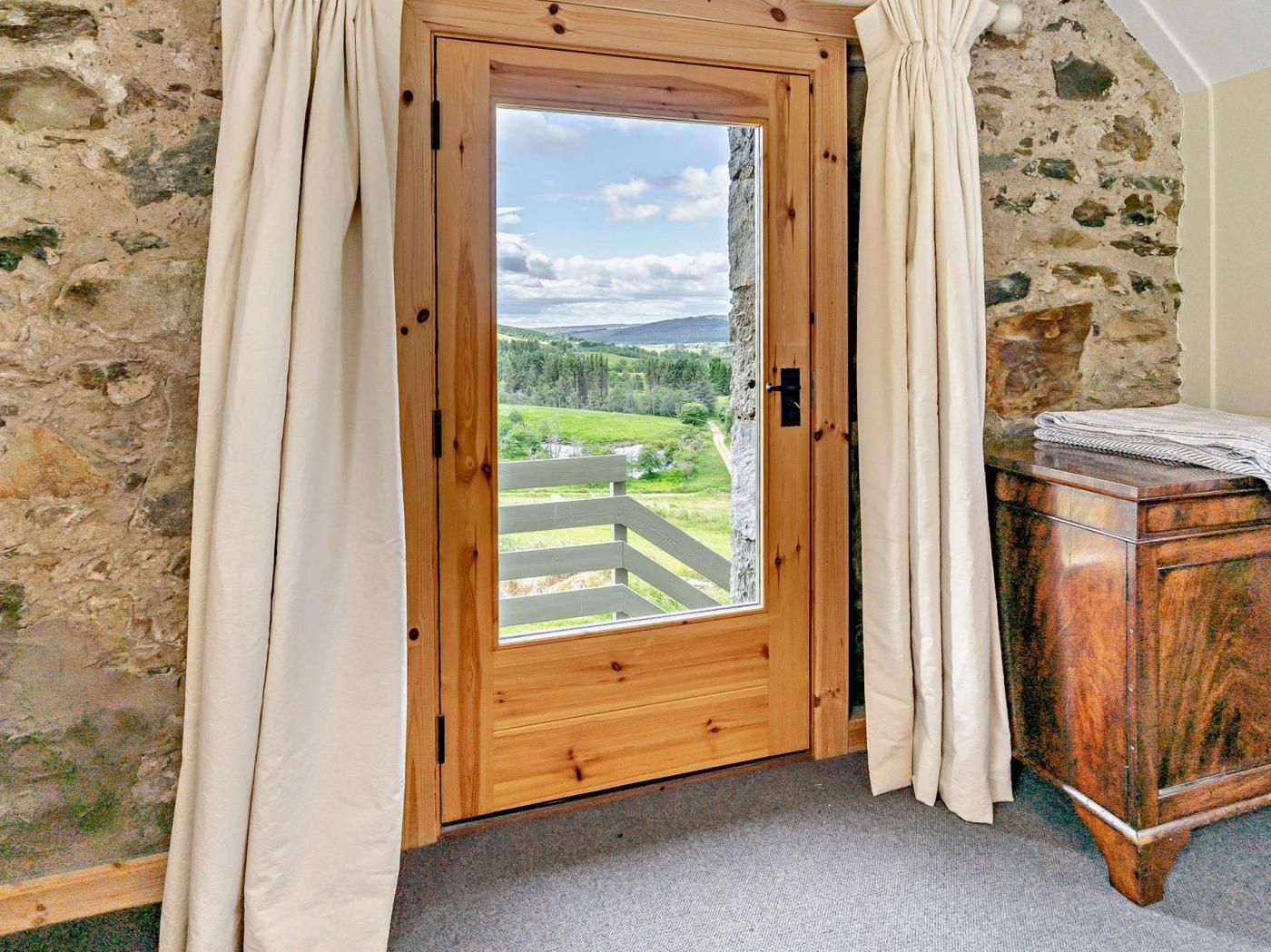 A wooden door with a view of a green landscape, a stone wall, and a wooden cabinet.
