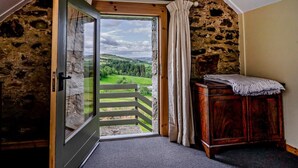 Une pièce avec un mur en pierre, une porte en bois donnant sur un balcon et un petit meuble en bois.