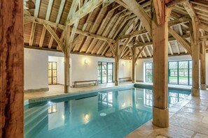 En indendørs swimmingpool med træloft og store vinduer.