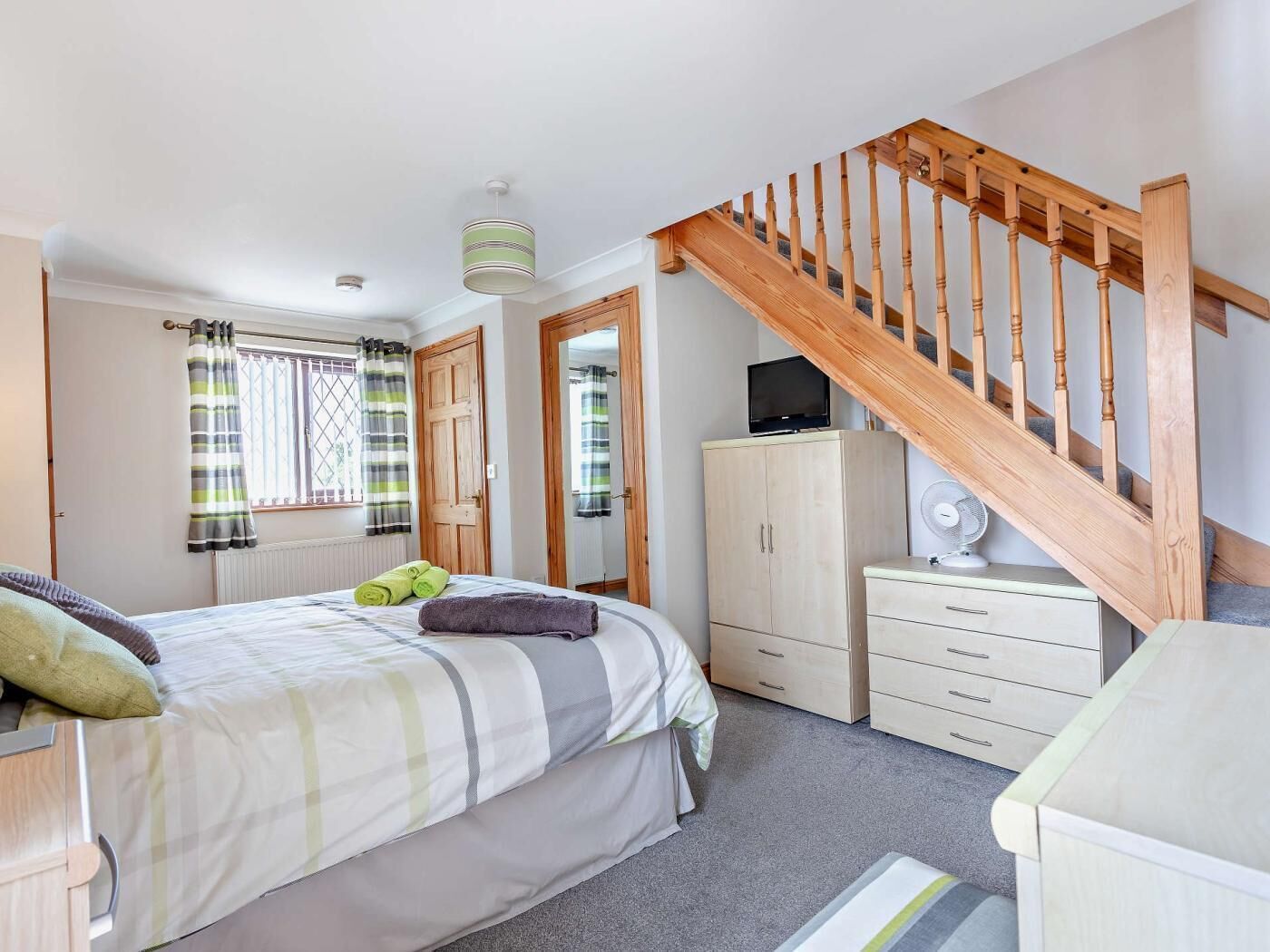 A bedroom with a bed, a wooden staircase, a wardrobe, and a television.