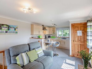A cozy living area with a grey sofa, a dining table, and a kitchen in the background. - 1 Bed in Bude (oc-96269) (Bude)