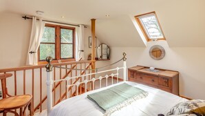 Una camera da letto con un letto, una cassettiera in legno, una finestra con tende, un lucernario e una ringhiera in legno.