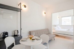 Quarto moderno com cama, mesa de jantar com cadeiras, sofá e cozinha compacta.