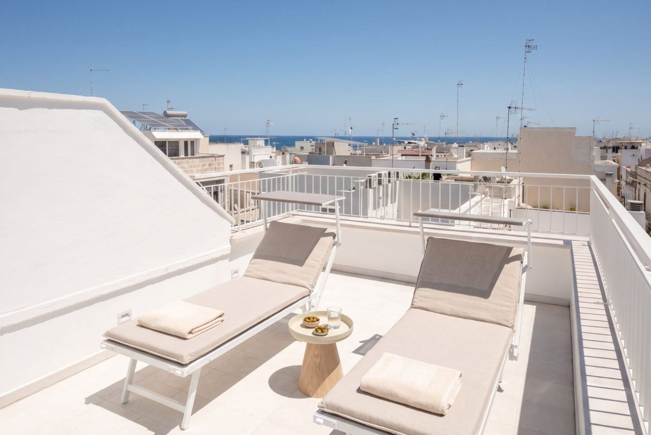 Een dak terras met ligbedden, een tafel met een drankje en een helder uitzicht op de stad en zee.