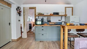 Een kleine keuken met een centraal kookeiland, een eettafel en een koelkast.