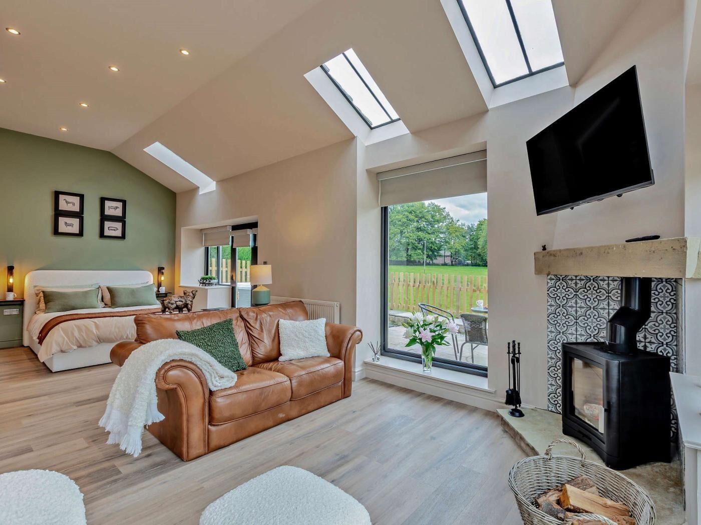 A modern living room with a sofa, a fireplace, a TV, and skylights.