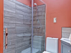 Ein modernes Badezimmer mit einer gläsernen Duschkabine, grauen Marmorfliesen, einer weißen Toilette und einem Waschbecken mit weißer Arbeitsplatte.