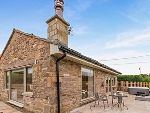 Ein Steinhaus mit Schornstein, großen Fenstern und einer Außenpatio-Terrasse mit Whirlpool und Sitzgelegenheiten.