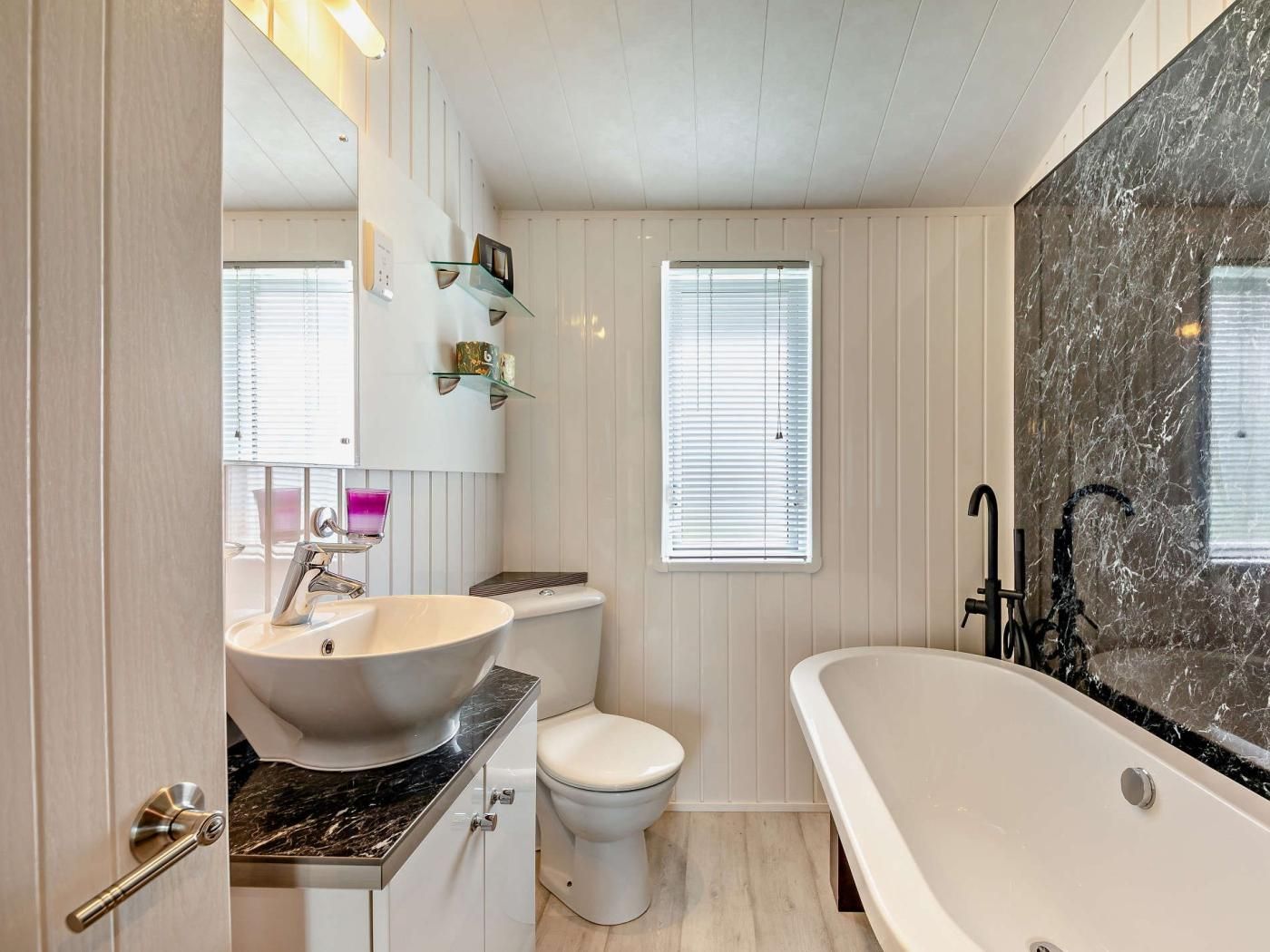 Ein Badezimmer mit einer freistehenden Badewanne, einer Toilette und einem Waschtisch mit Waschbecken und Spiegel.