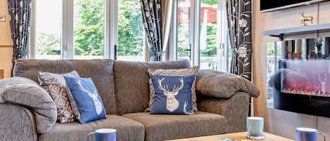 A cozy living room with a sofa, decorative pillows, a coffee table with pastries, and a fireplace.