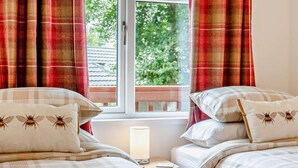 A bedroom with two beds, a nightstand, a lamp, and a window with curtains.