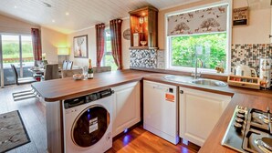 A kitchen with a dishwasher, stove, and a large window with a view of greenery.