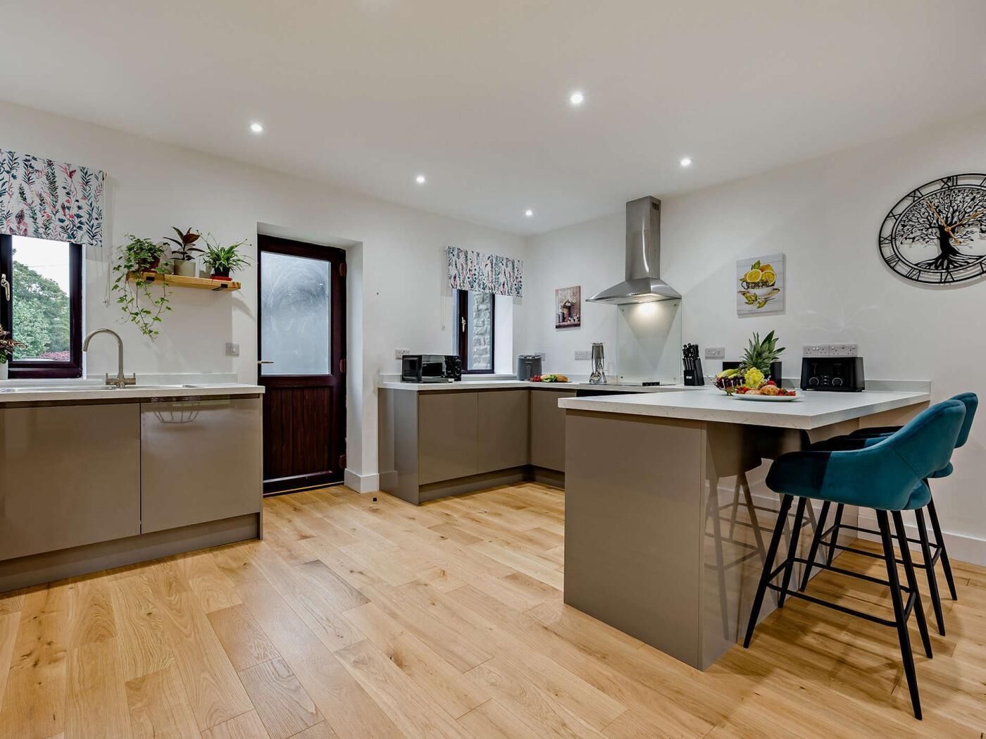 A modern kitchen with a central island, wooden flooring, and a clock on the wall.