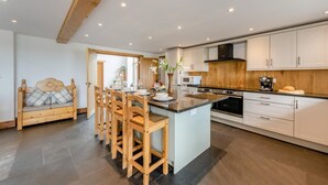 A modern kitchen with a central island, wooden chairs, and a dining table. - 6 Bed in Holsworthy (oc-lympb) (Bradworthy)