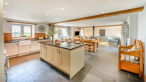 A spacious kitchen with a central island, dining area with wooden furniture, and a living room with a sofa and a TV. - 6 Bed in Holsworthy (oc-lympb) (Bradworthy)