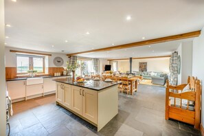 Eine geräumige Küche mit Kochinsel, ein Essbereich mit Holzmöbeln und ein Wohnzimmer mit Sofa und Fernseher.