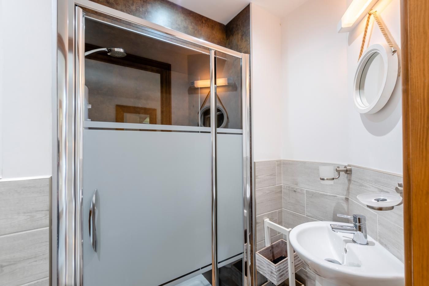 Un baño moderno con ducha envuelta en vidrio, un lavamanos blanco y un espejo en la pared.