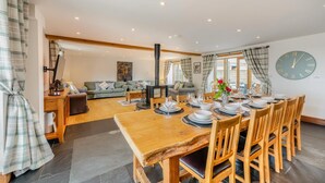 A dining area with a wooden table set for four, a sofa, a fireplace, and a clock on the wall. - 6 Bed in Holsworthy (oc-lympb) (Bradworthy)
