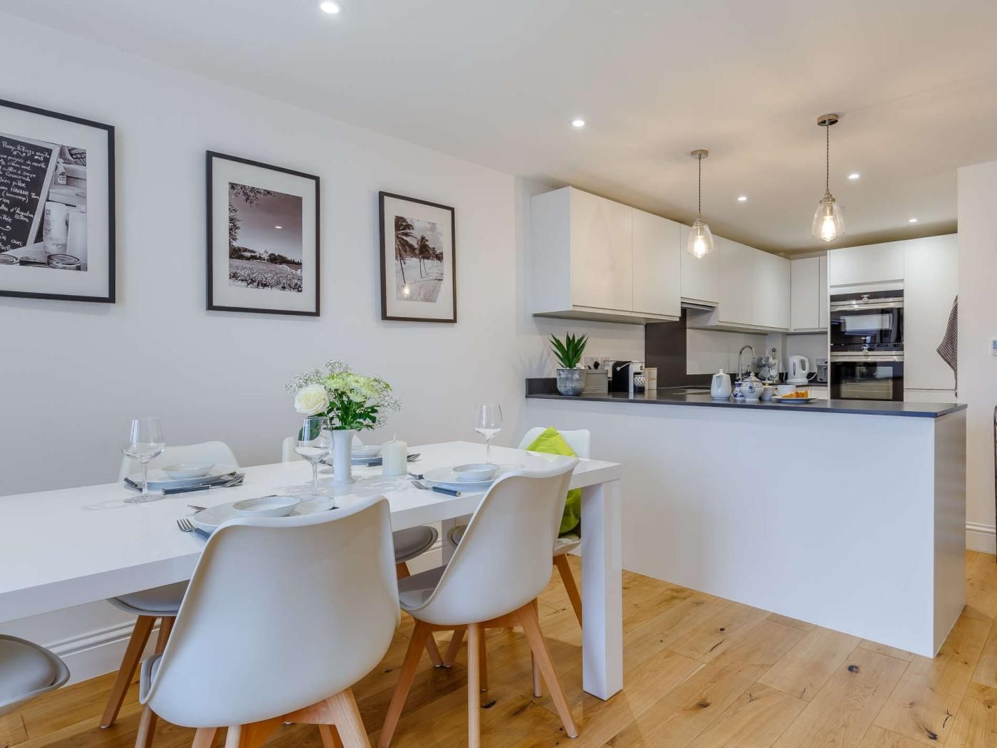 A modern kitchen with white cabinets, a central island, and a dining area with a white table and chairs.