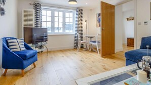 Ein modernes Wohnzimmer mit Fernseher, blauen Sesseln, einem Couchtisch und einem Essbereich mit Tisch und Stühlen.