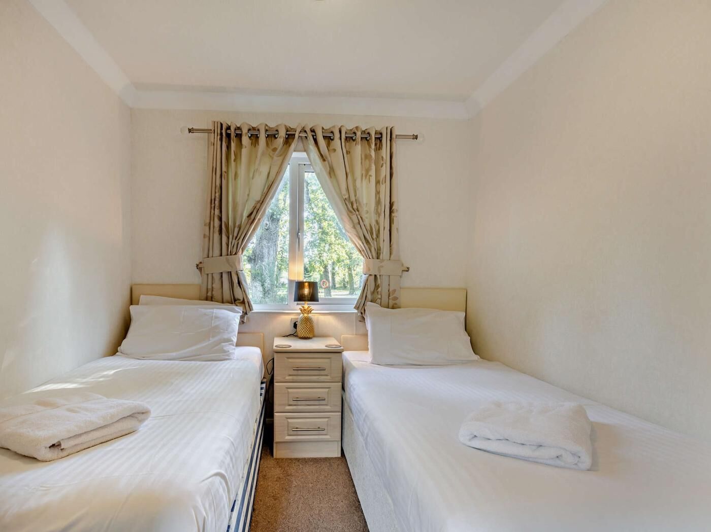 Une chambre avec deux lits, une table de chevet avec une lampe et une fenêtre avec des rideaux.