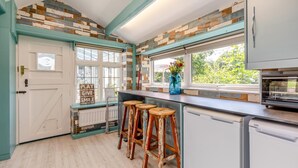 Een keuken met een witte deur, een raam met uitzicht, een blauwe vaas met bloemen en een inbouwoven.