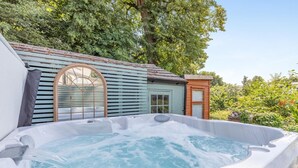 Een hottub met een houten terras en een klein gebouw met raam en deur.
