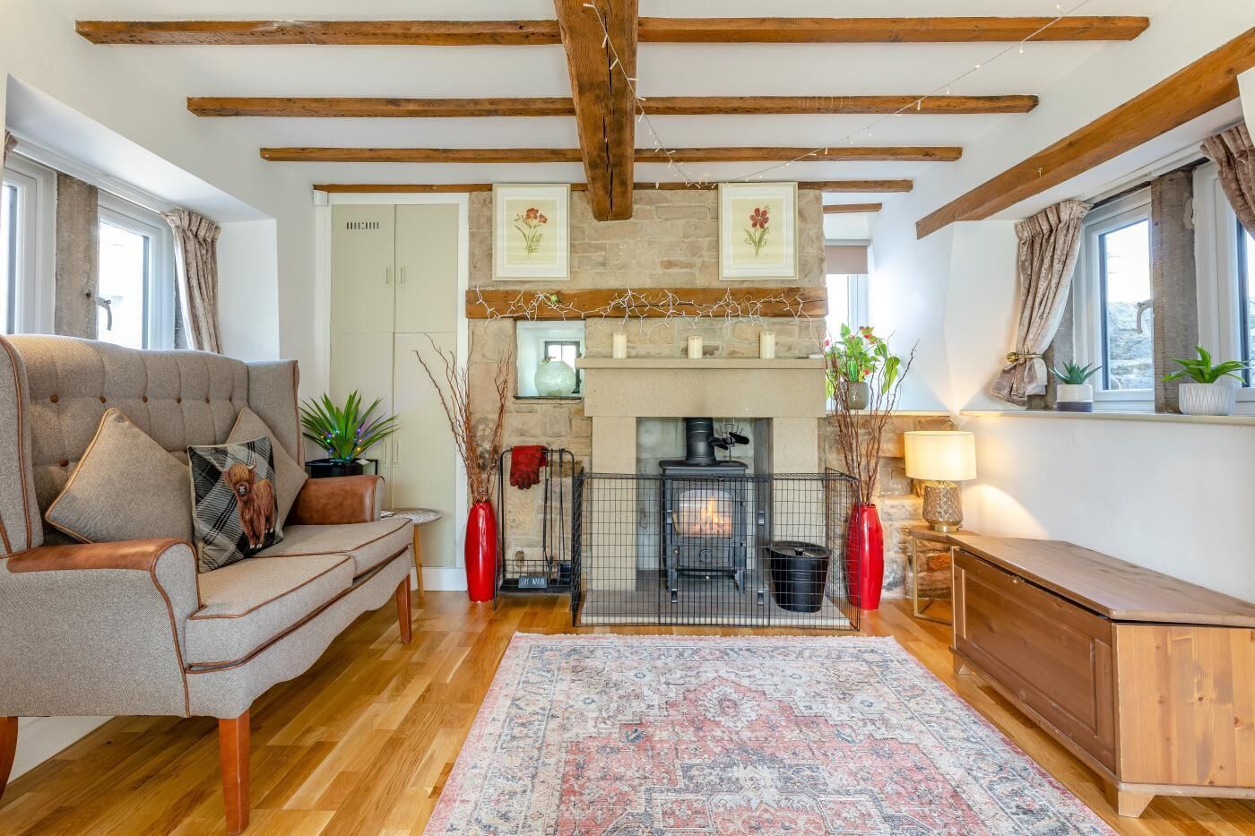 A cozy living room with a fireplace, wooden beams, a sofa, and a rug.