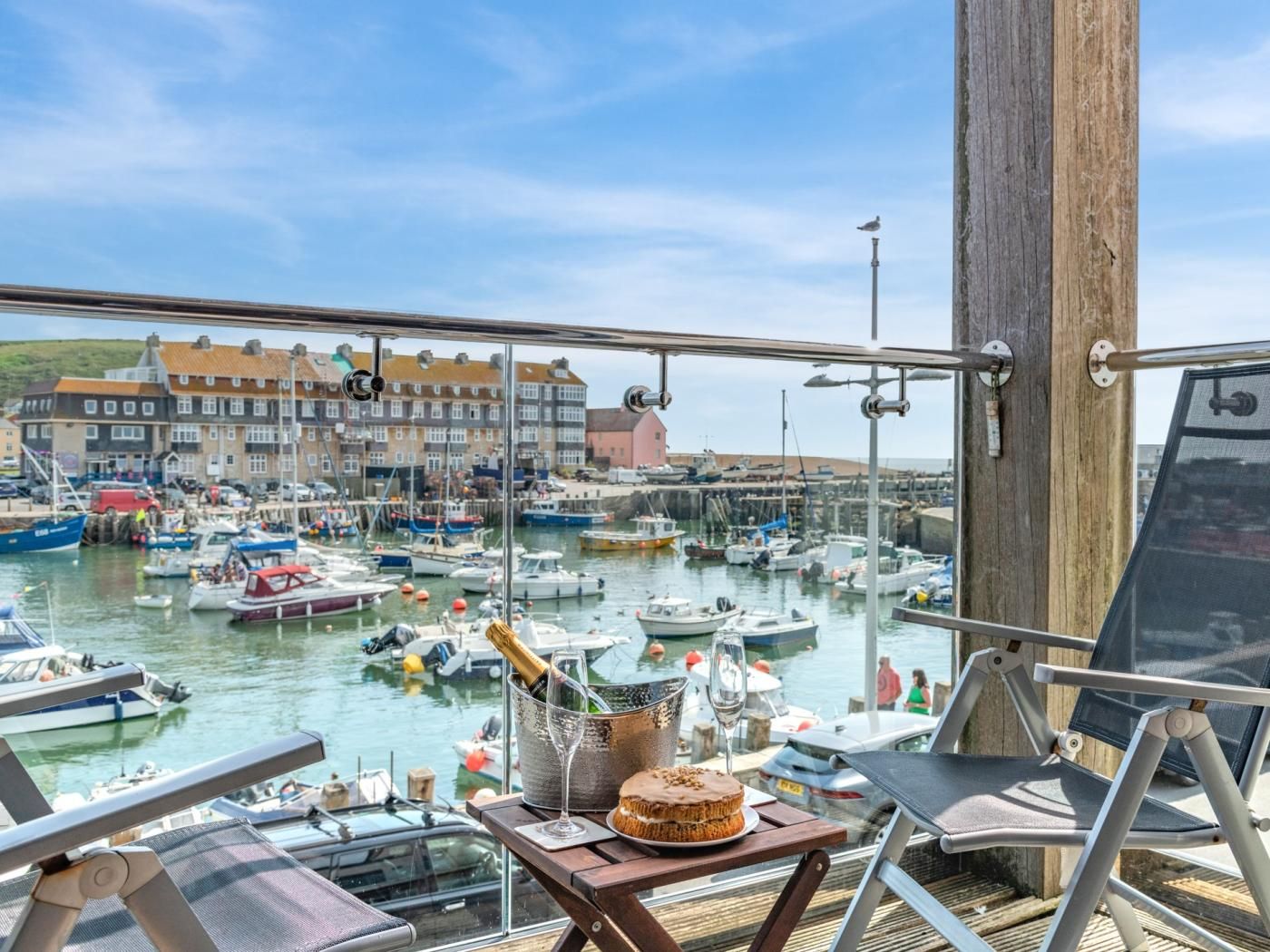 Un balcon donnant sur un port de plaisance, une bouteille de champagne et un gâteau sur une table.
